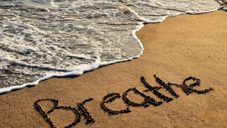 the word breathe written on a sandy beach